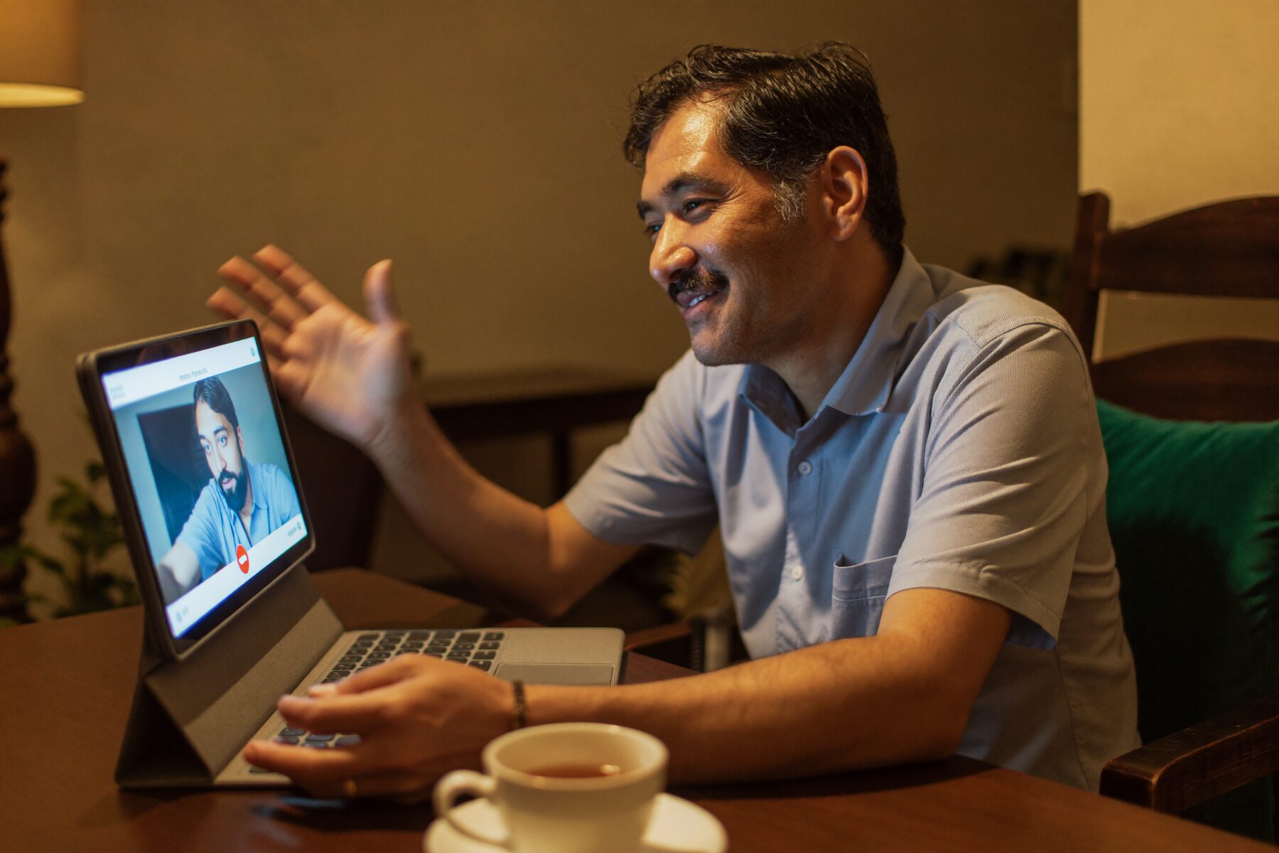 A father listens on a video call at his kitchen table in the evening.