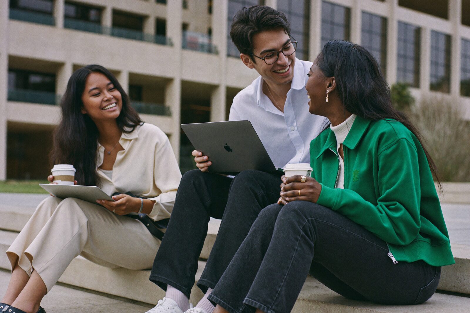 Three students talking on the steps outside a university library.