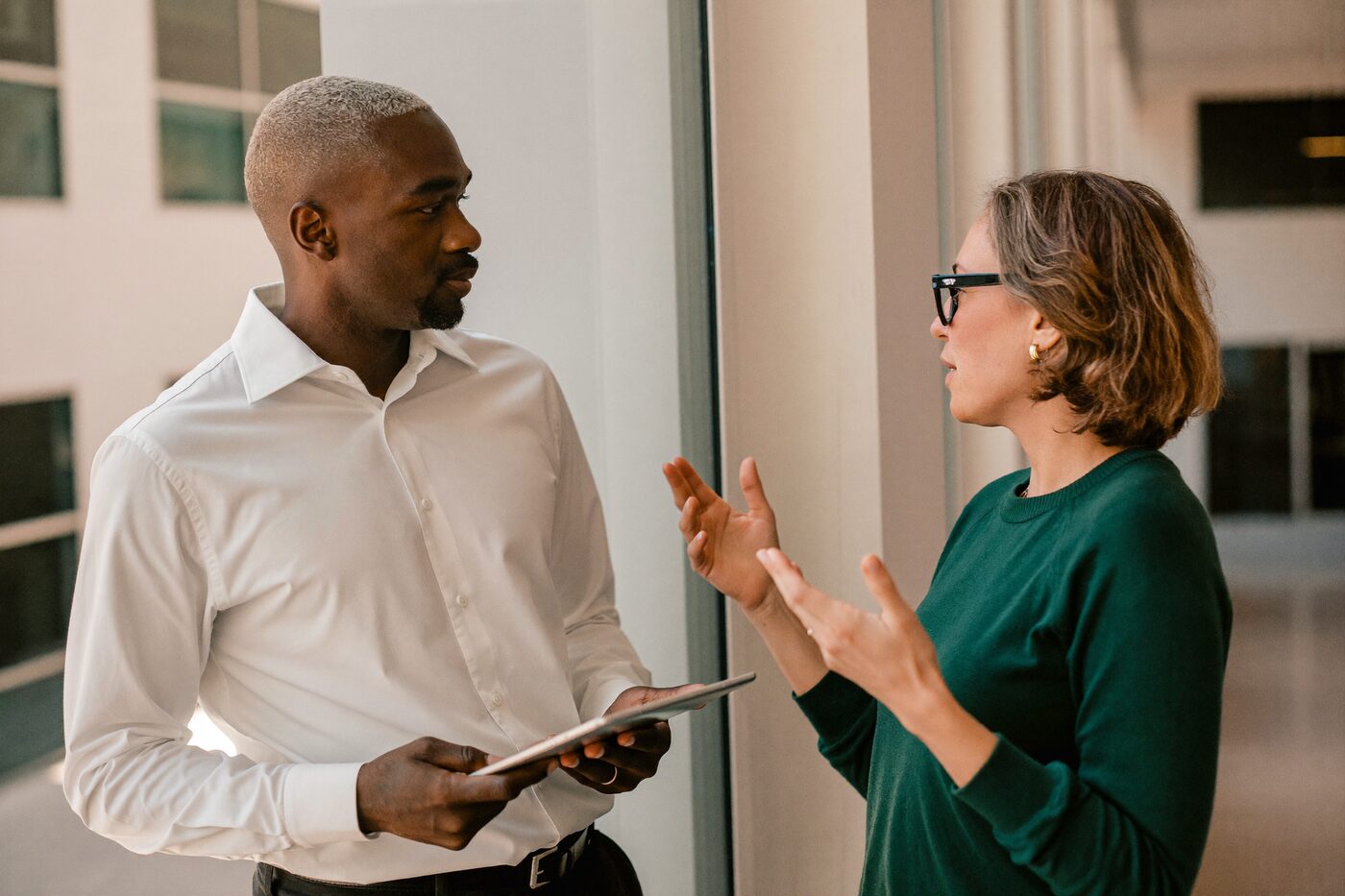 Two university staff in conversation beside a tall window.